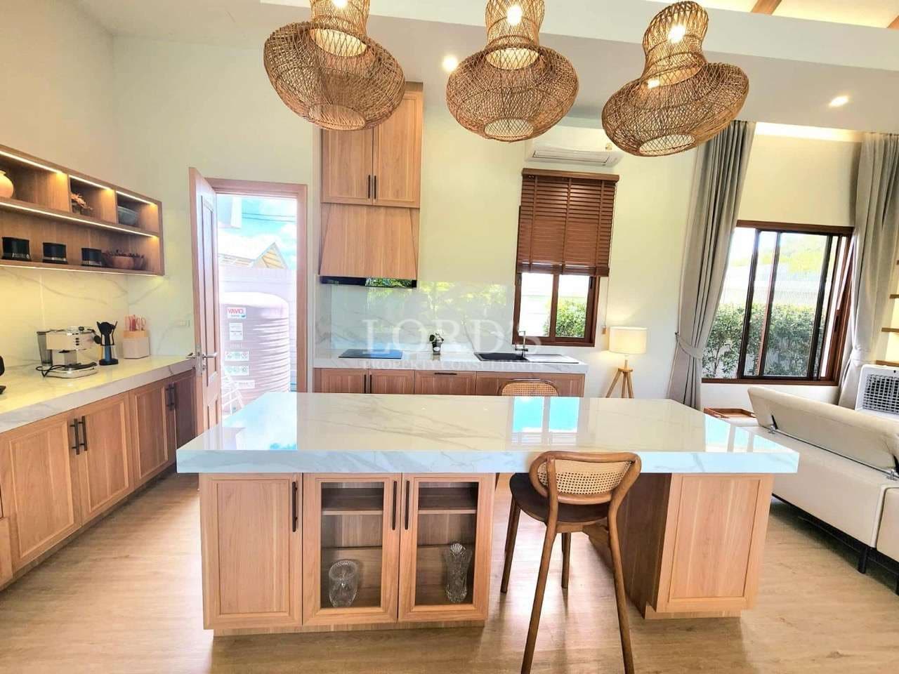 Modern open-plan kitchen with marble island, wooden cabinets, pendant lights, and bar seating