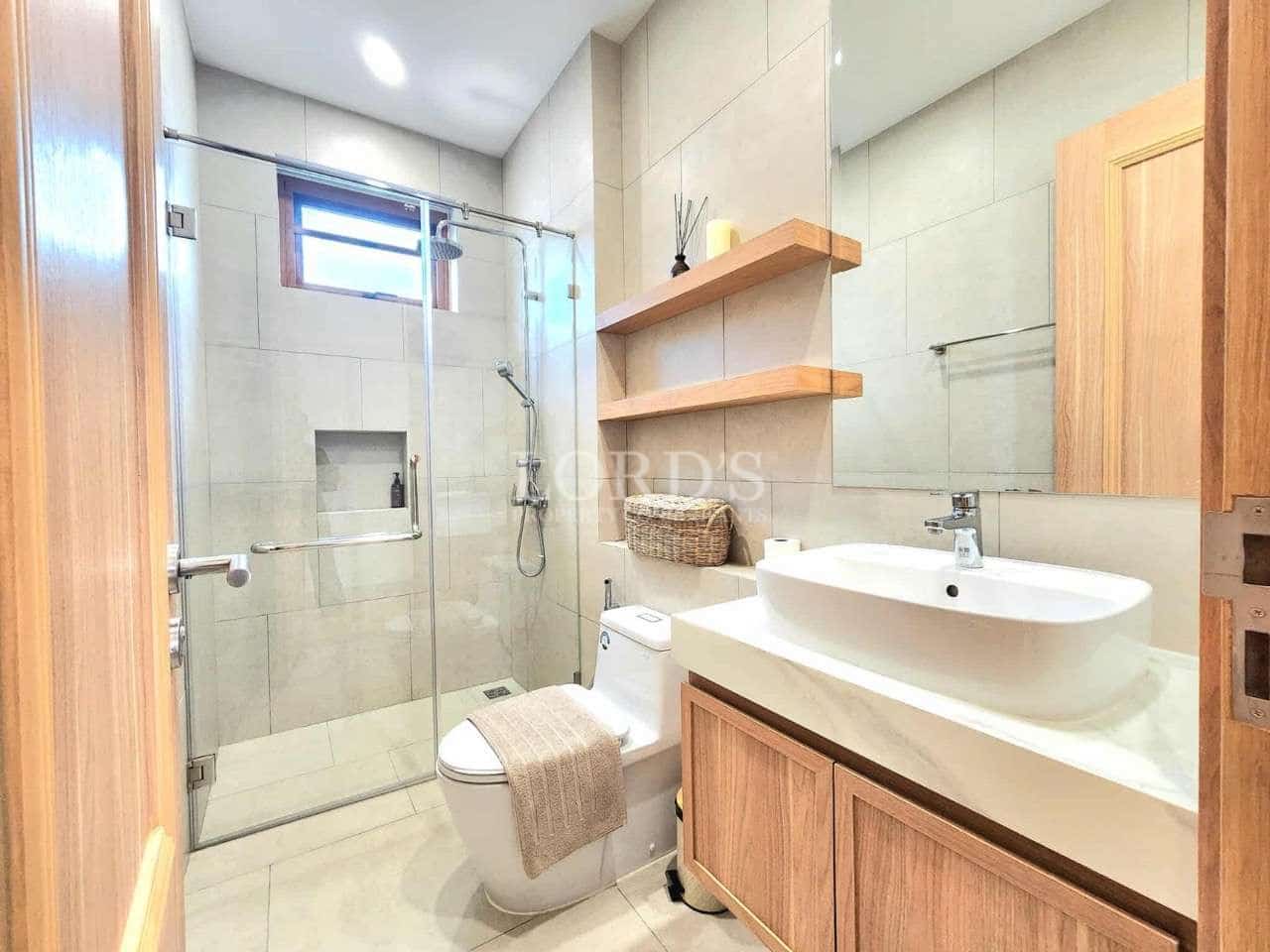 Modern bathroom with glass shower enclosure, wooden vanity, floating shelves, and ceramic sink