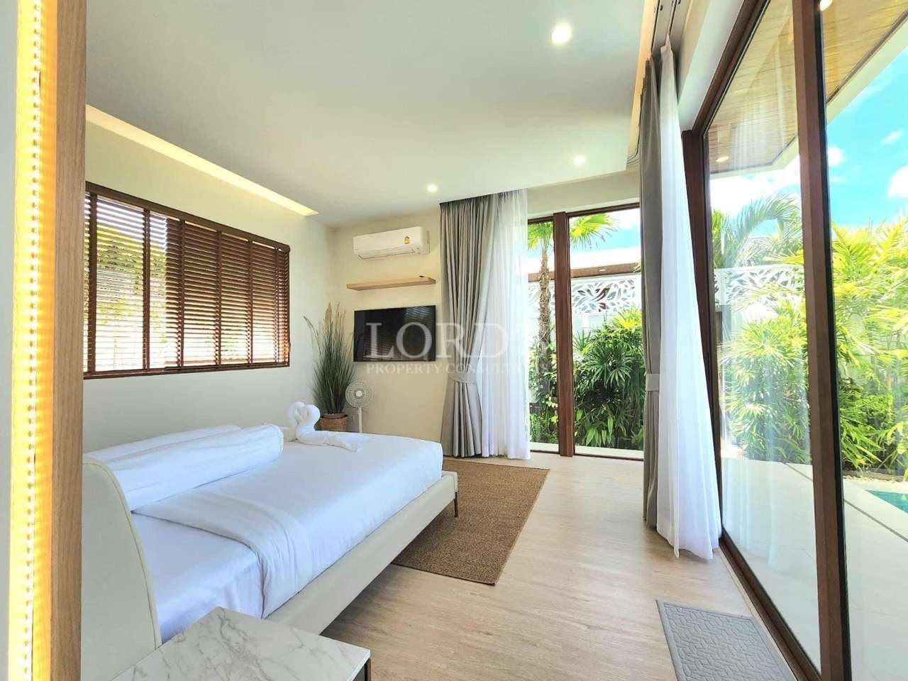 Bright modern bedroom with king-size bed, floor-to-ceiling glass doors, wooden blinds, and garden view
