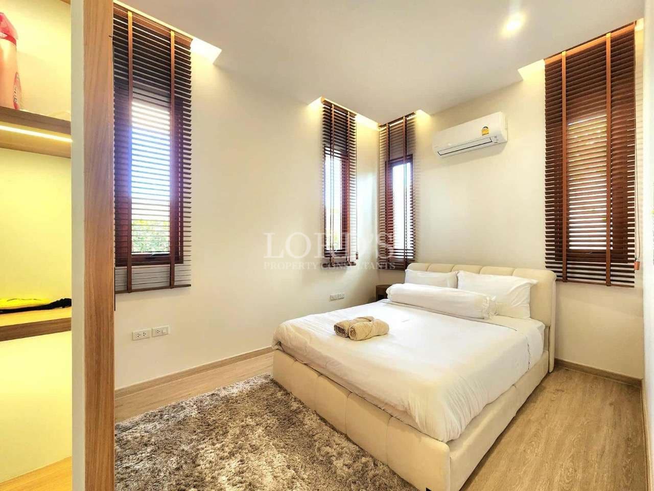 Modern bedroom with neutral decor, wooden blinds, built-in shelving, and soft ambient lighting