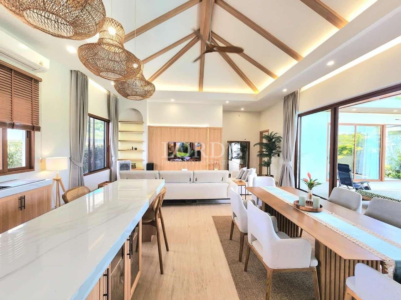 Open-plan living, dining, and kitchen area with high vaulted ceiling, wooden beams, and sliding glass doors