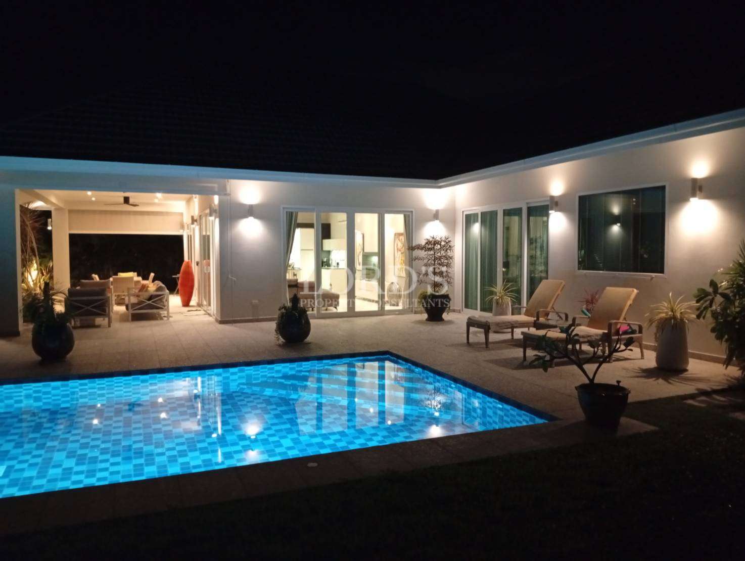 Modern villa with an illuminated swimming pool and outdoor seating area at night.