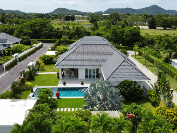Aerial view of a modern villa with a private swimming pool, green lawn, and mountain views in a quiet residential neighborhood.