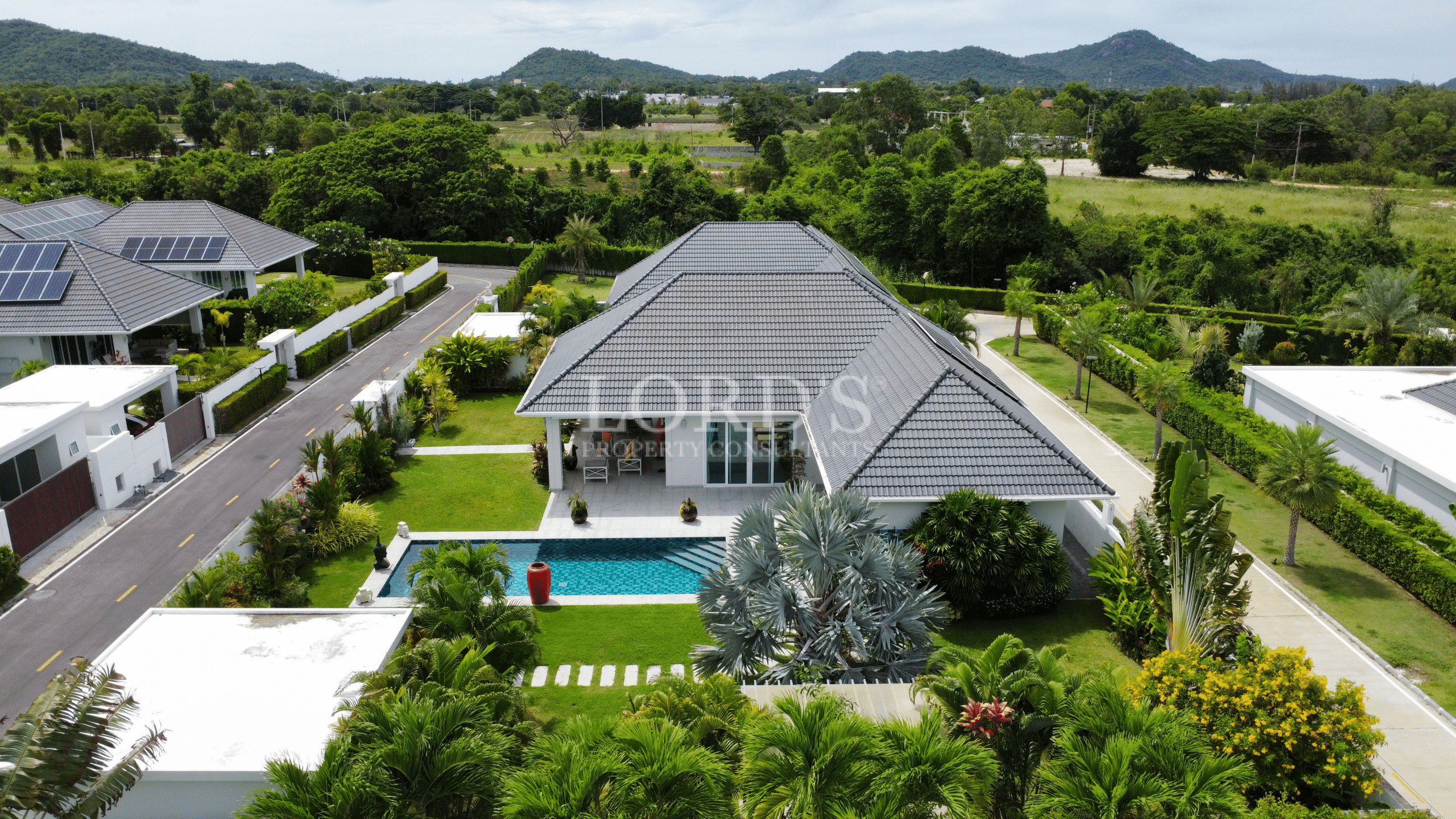 Aerial view of a modern villa with a private swimming pool, green lawn, and mountain views in a quiet residential neighborhood.