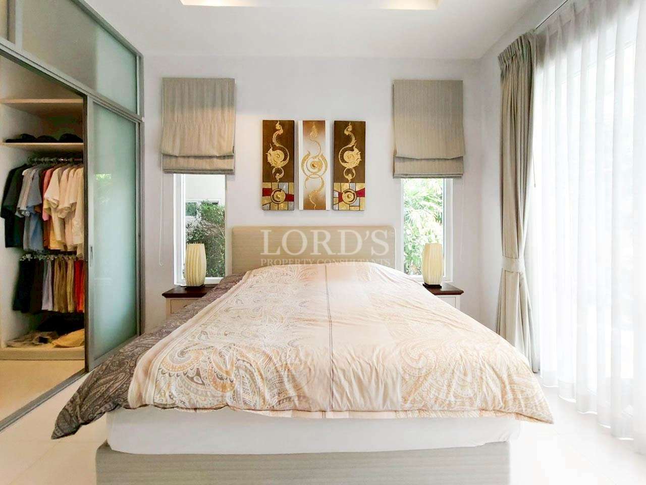 Bright modern bedroom with upholstered bed, walk-in closet, and large window with sheer curtains