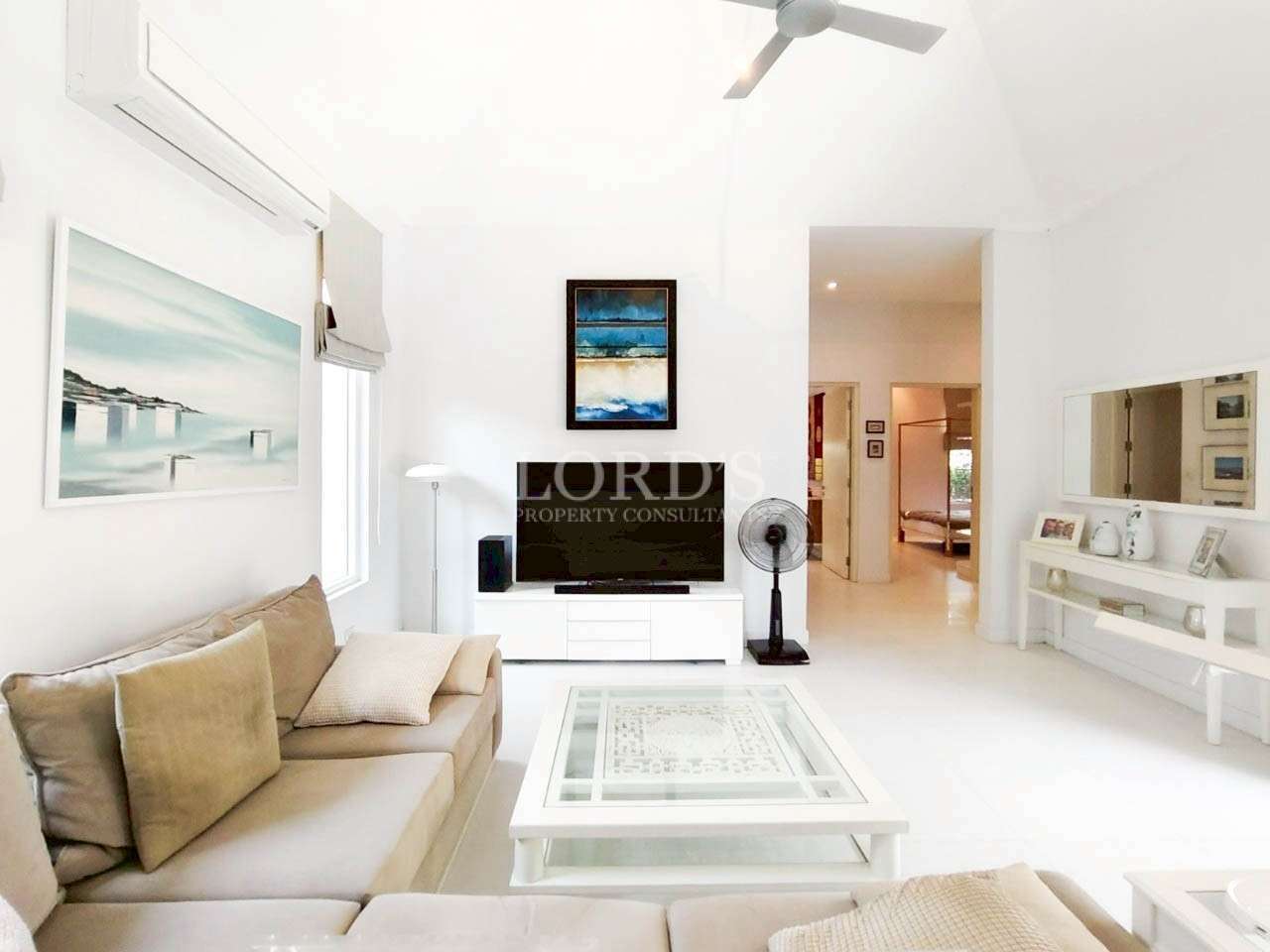 Bright modern living room with white interior, TV unit, ceiling fan, and neutral sofa