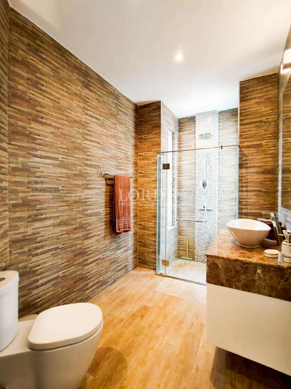 Modern bathroom with glass shower enclosure, stone tile walls, and wooden flooring