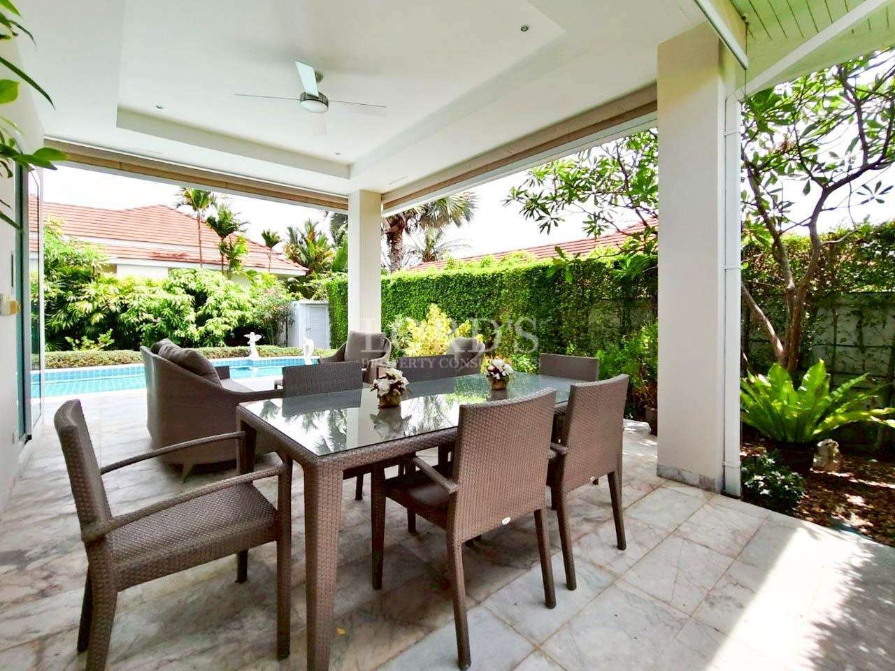 Covered outdoor dining area with wicker table and chairs beside a private villa swimming pool.