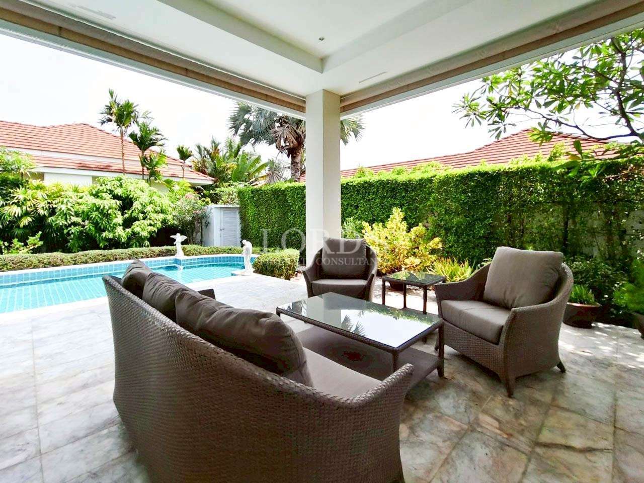 Covered villa patio with wicker seating set overlooking a private swimming pool and garden.