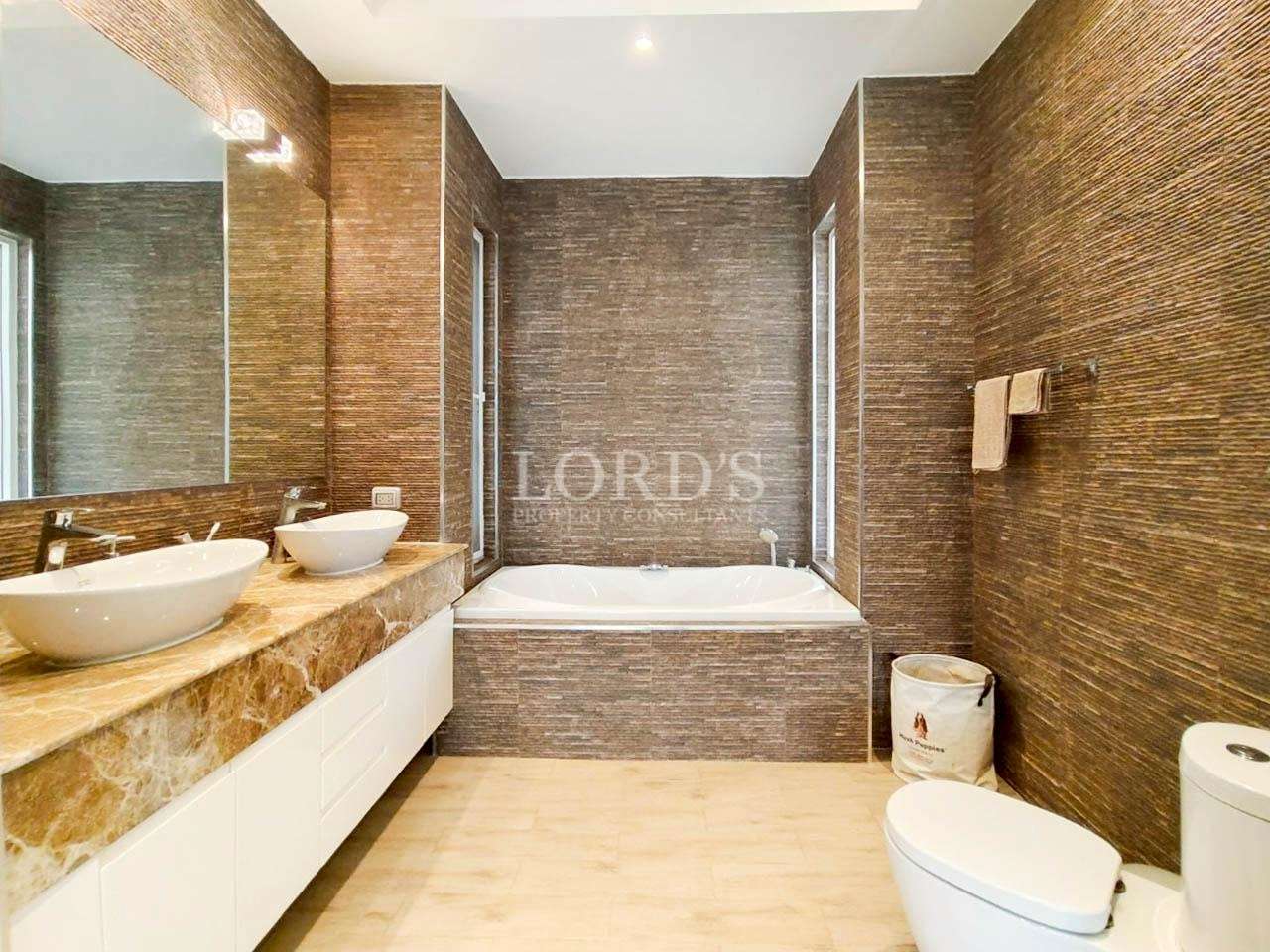 Luxury bathroom with double vessel sinks, marble vanity, textured stone walls, and built-in bathtub