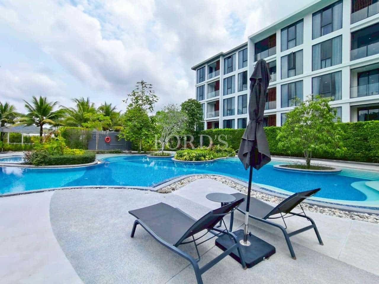 Modern condominium swimming pool with sun loungers and landscaped gardens.