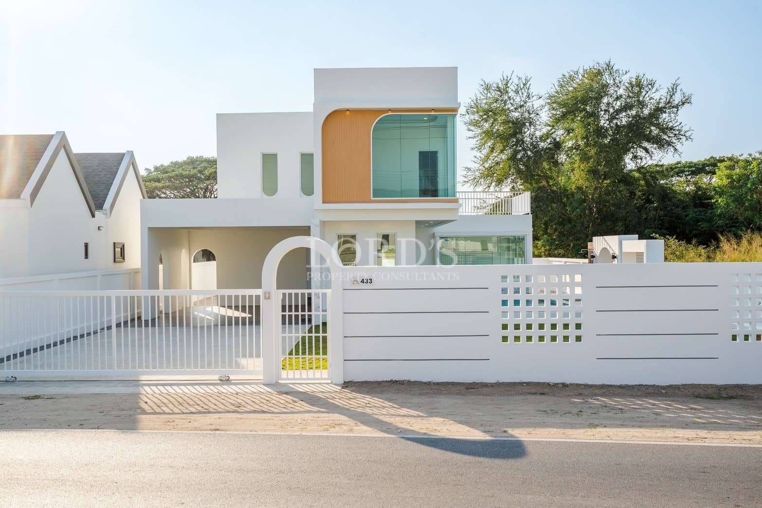 Modern two-story house with white exterior, curved windows, and gated front entrance