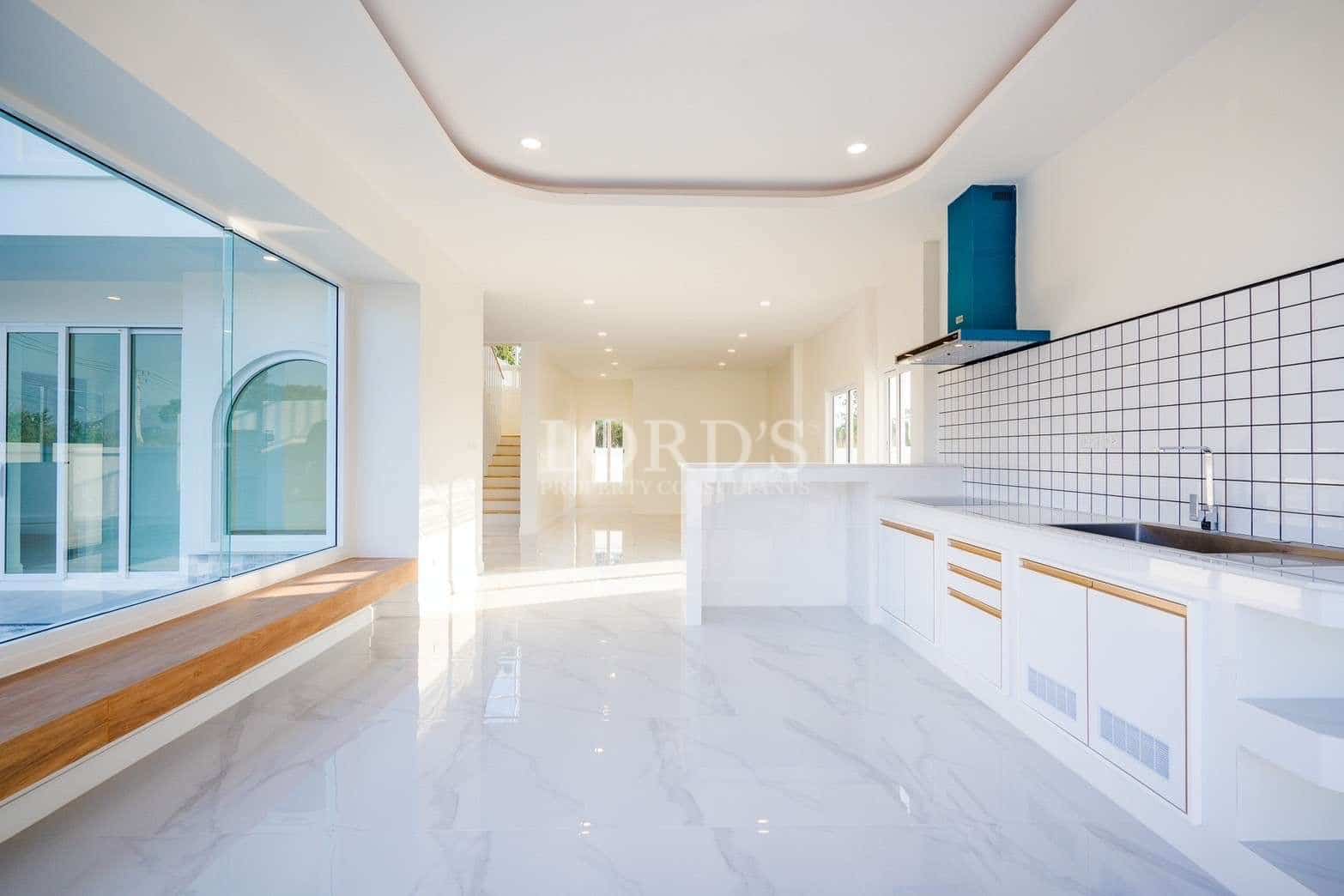 Bright modern kitchen with white cabinets, tiled backsplash, and large glass window seating area