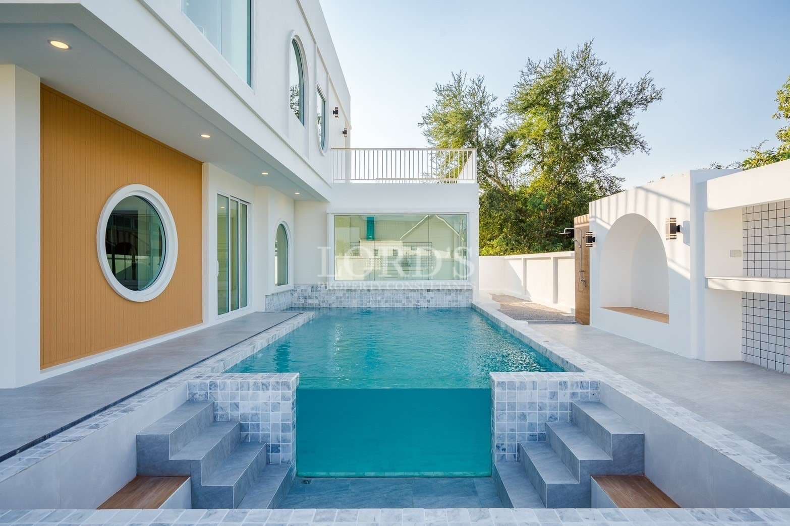Modern private swimming pool with tiled steps beside a contemporary two-story house