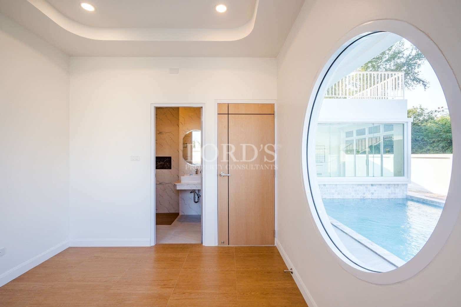 Modern bedroom with oval window overlooking private swimming pool and en-suite bathroom