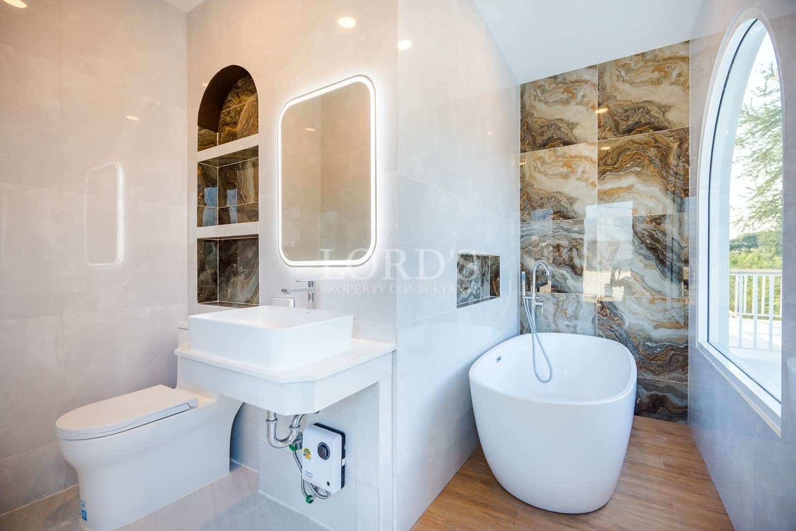 Modern luxury bathroom with freestanding bathtub, LED mirror, and marble accent wall