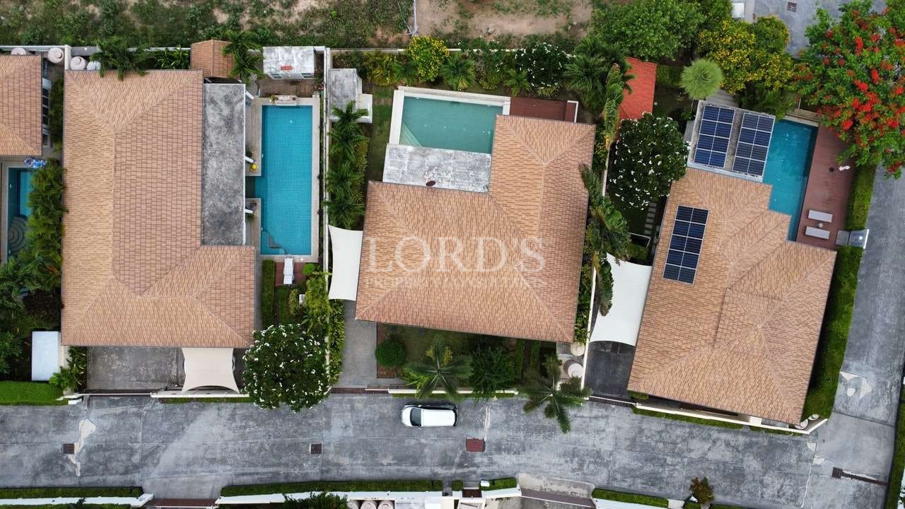 Top-down aerial view of modern villas with terracotta roofs, private swimming pools, landscaped gardens, and solar panels. Caption: