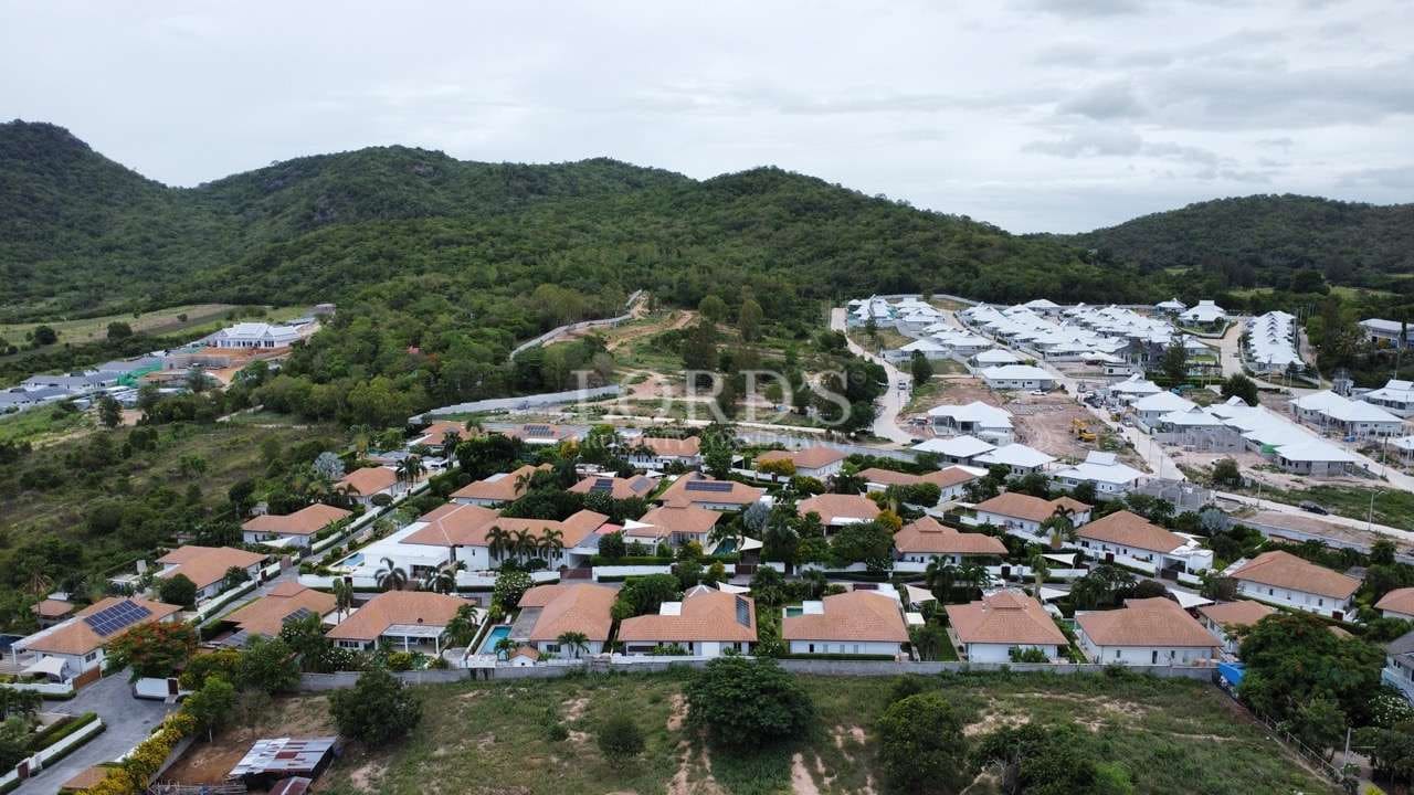Aerial view of a planned residential community with terracotta-roof villas, green hills, and nearby housing development.