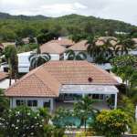 Aerial view of modern villas with terracotta roofs, private swimming pools, and lush tropical greenery surrounded by hills.