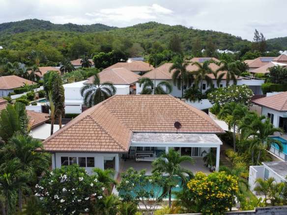 Aerial view of modern villas with terracotta roofs, private swimming pools, and lush tropical greenery surrounded by hills.
