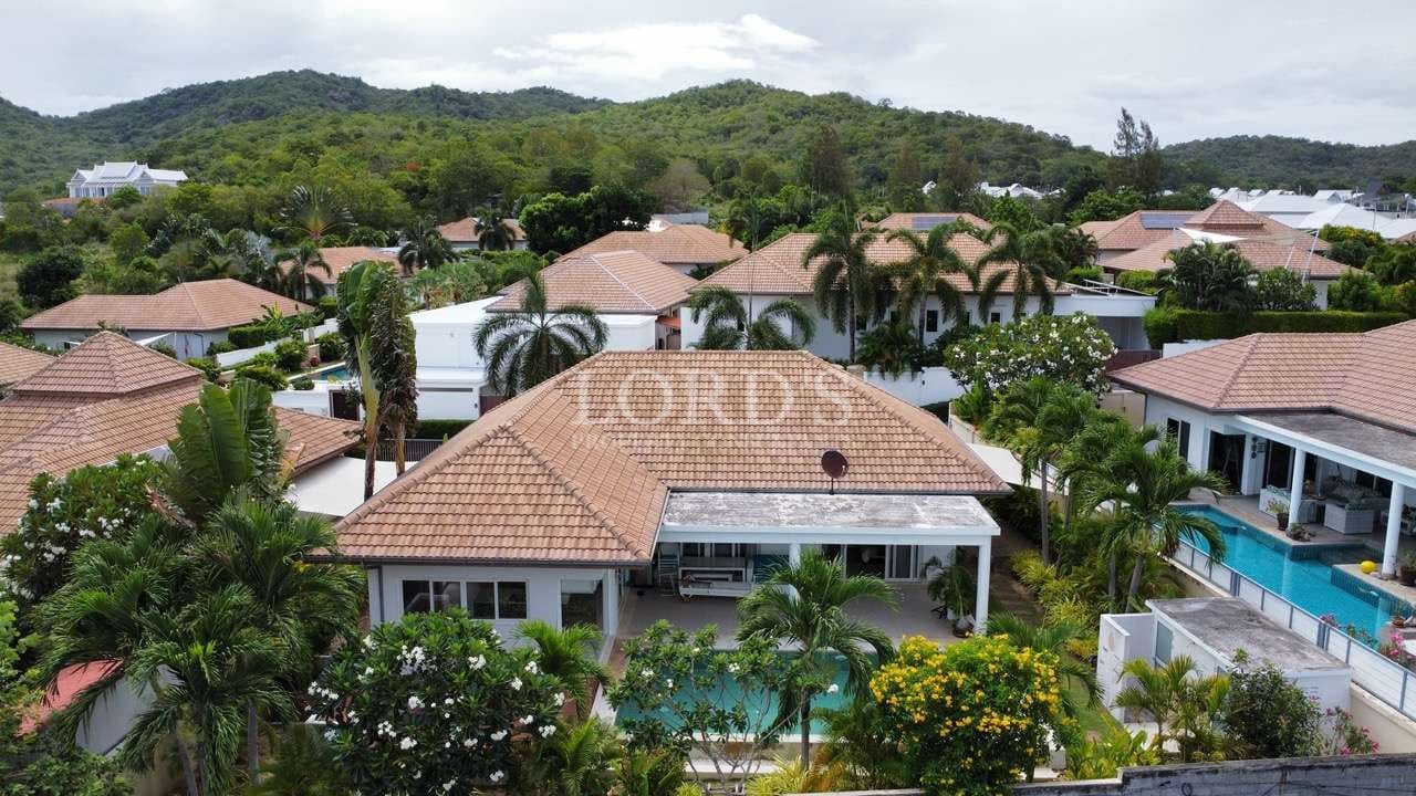 Aerial view of modern villas with terracotta roofs, private swimming pools, and lush tropical greenery surrounded by hills.