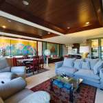 Open-plan living and dining area with wooden ceiling, modern sofas, and decorative wall art