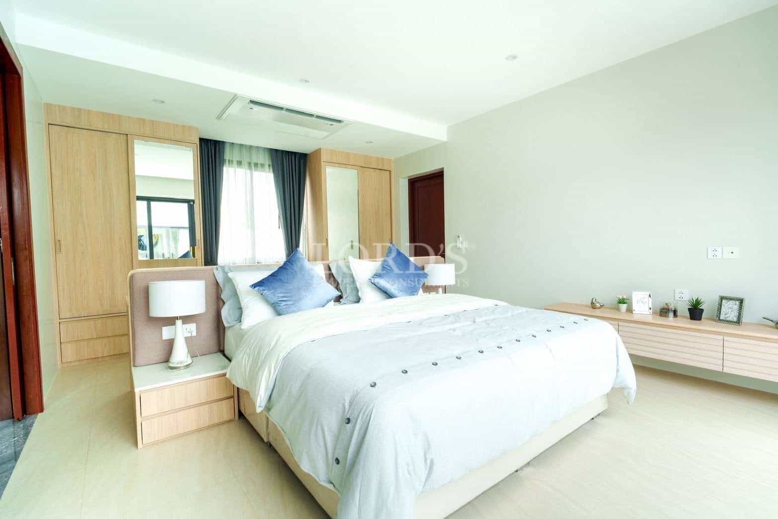 Modern bedroom with king-size bed, built-in wooden wardrobe, soft lighting, and minimalist décor.