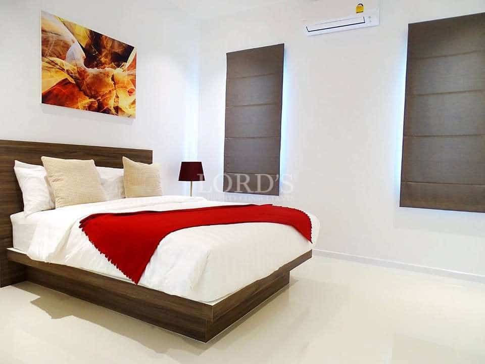 Modern minimalist bedroom with wooden bed, white bedding, red throw, and wall art