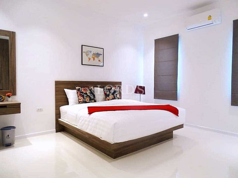 Modern minimalist bedroom with wooden bed frame, white walls, and air conditioning