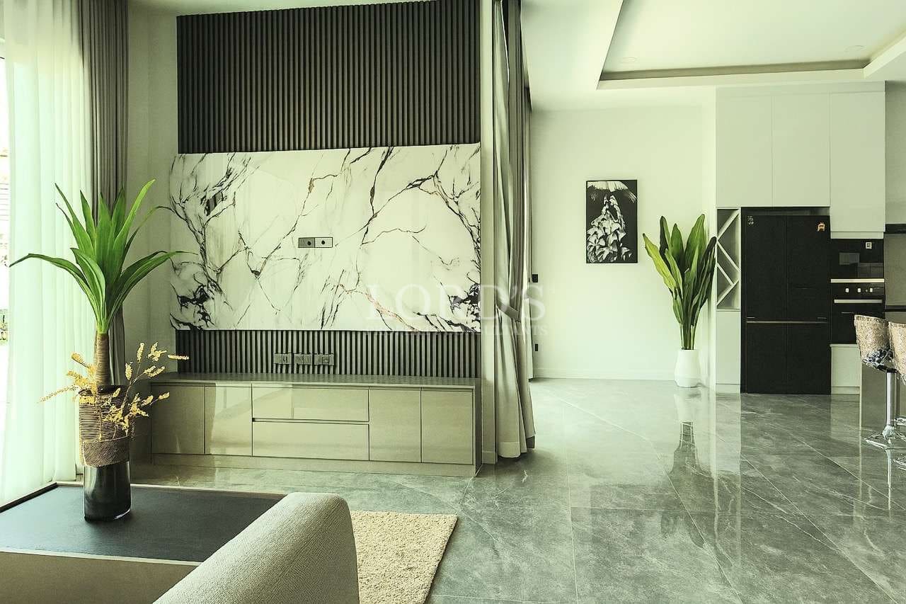 Modern open-plan living room with marble accent wall, indoor plants, and contemporary kitchen design