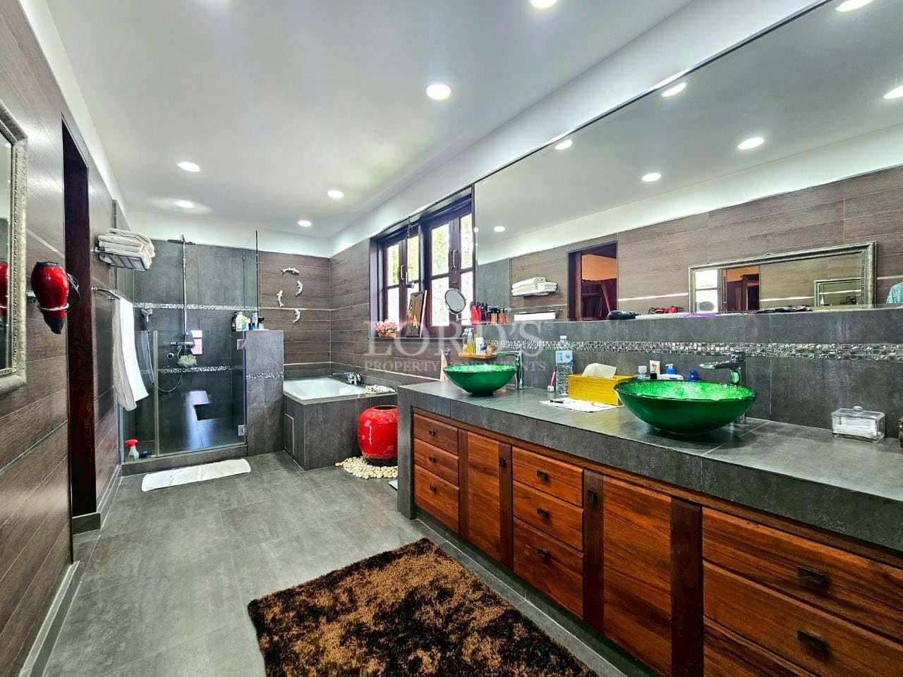 Luxury bathroom with double vanity, green vessel sinks, walk-in shower, bathtub, and modern lighting