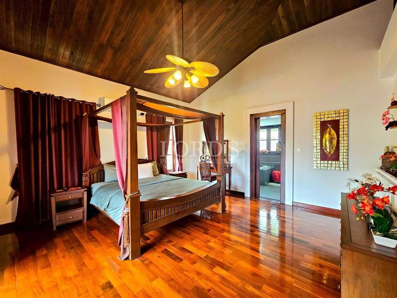 Elegant bedroom with wooden four-poster bed, polished hardwood floors, vaulted ceiling, and warm lighting