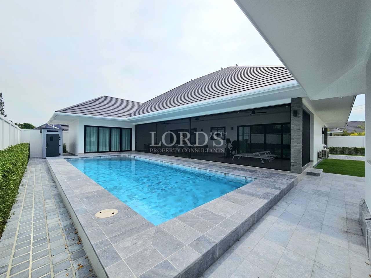 Private swimming pool with modern villa, covered terrace, and outdoor lounge area