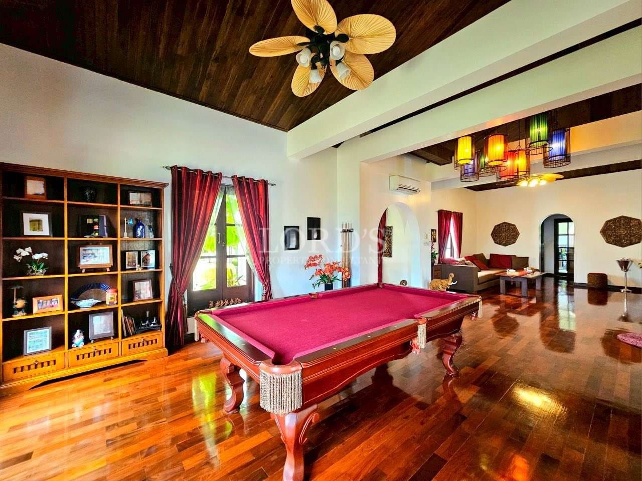 Luxury living room with pool table, polished wooden floors, red curtains, and colorful pendant lighting