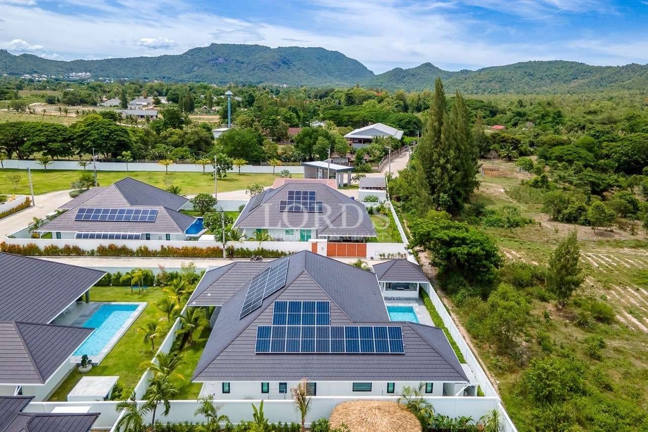 Aerial view of modern villas with solar panels, private pools, and green mountain surroundings