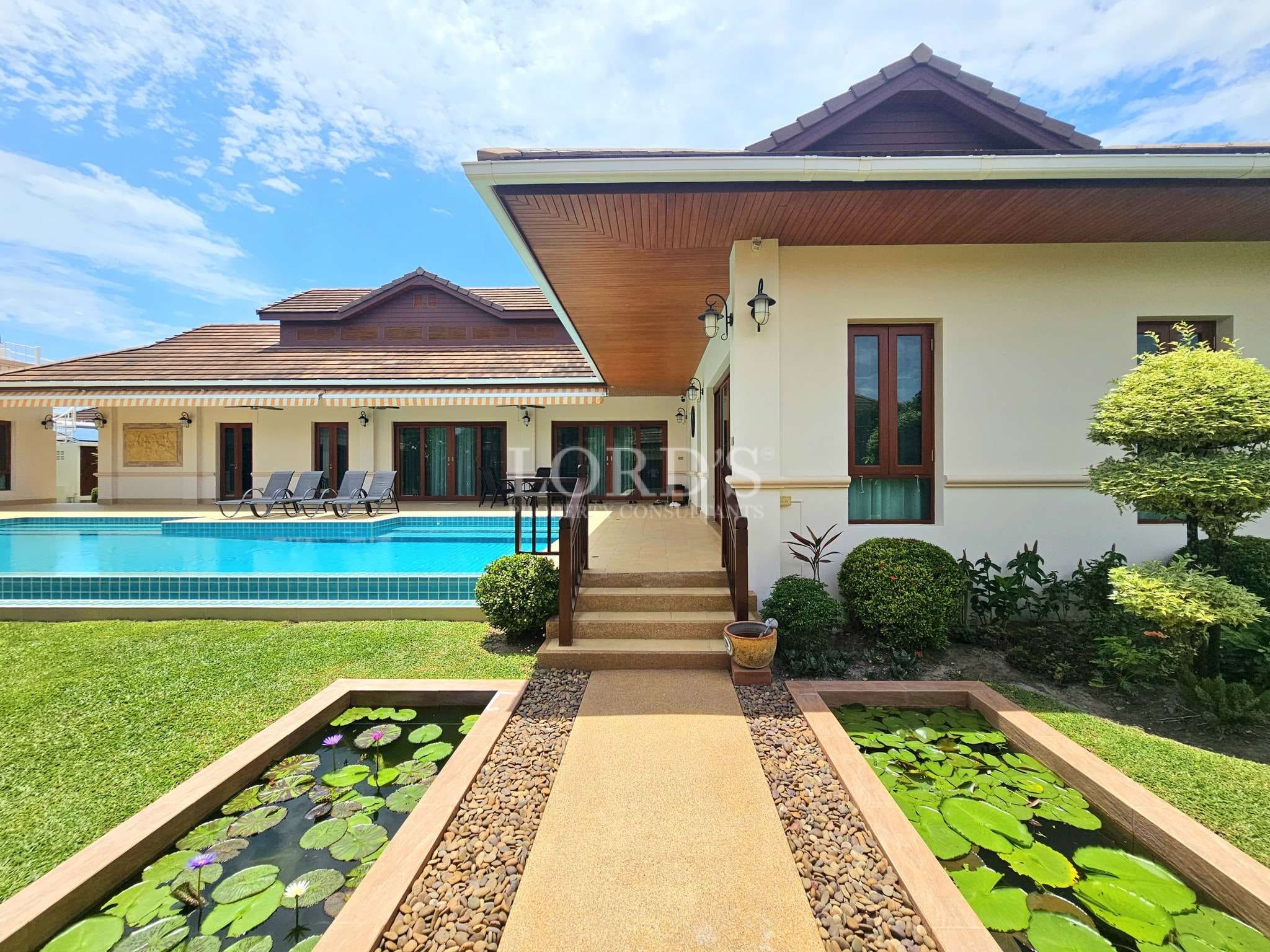 Luxury villa exterior with swimming pool, garden walkway, and decorative water features