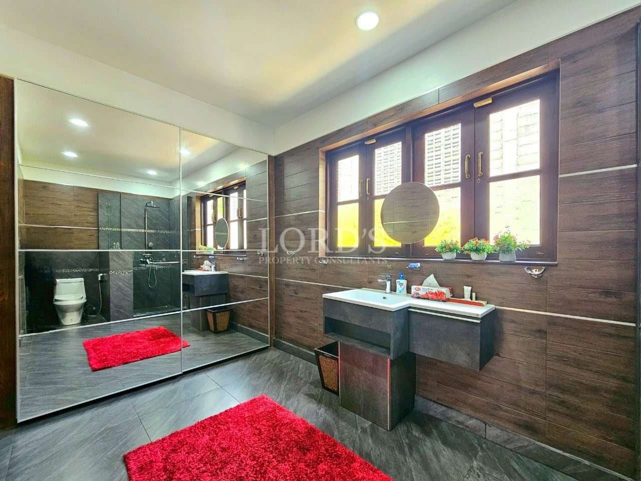 Spacious modern bathroom with wooden wall tiles, large mirror, vanity sink, and walk-in glass shower.