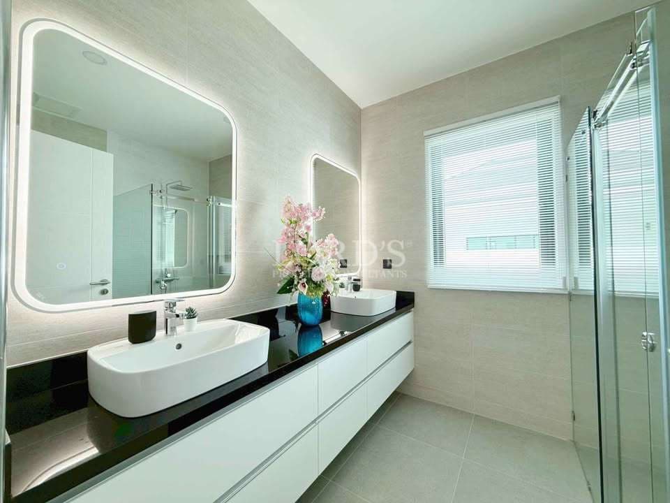 Modern bathroom with double sink vanity, LED backlit mirrors, glass shower enclosure, and neutral tiles.