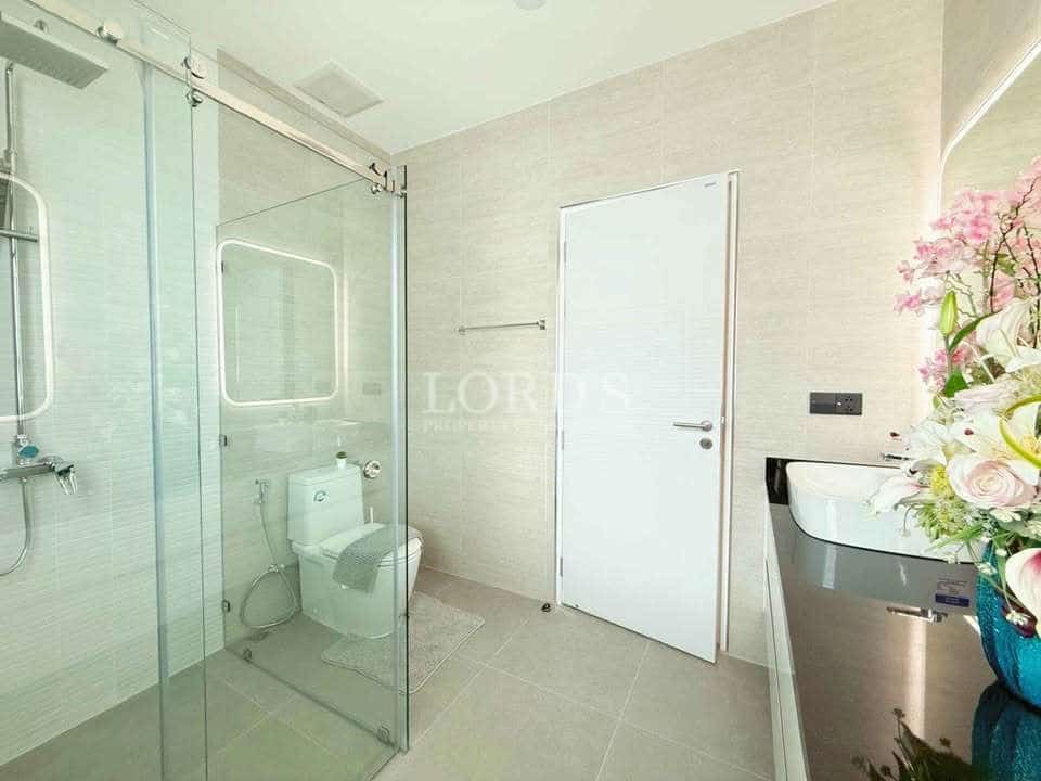 Modern bathroom with glass shower enclosure, wall-mounted sink, neutral tiles, and minimalist interior design.