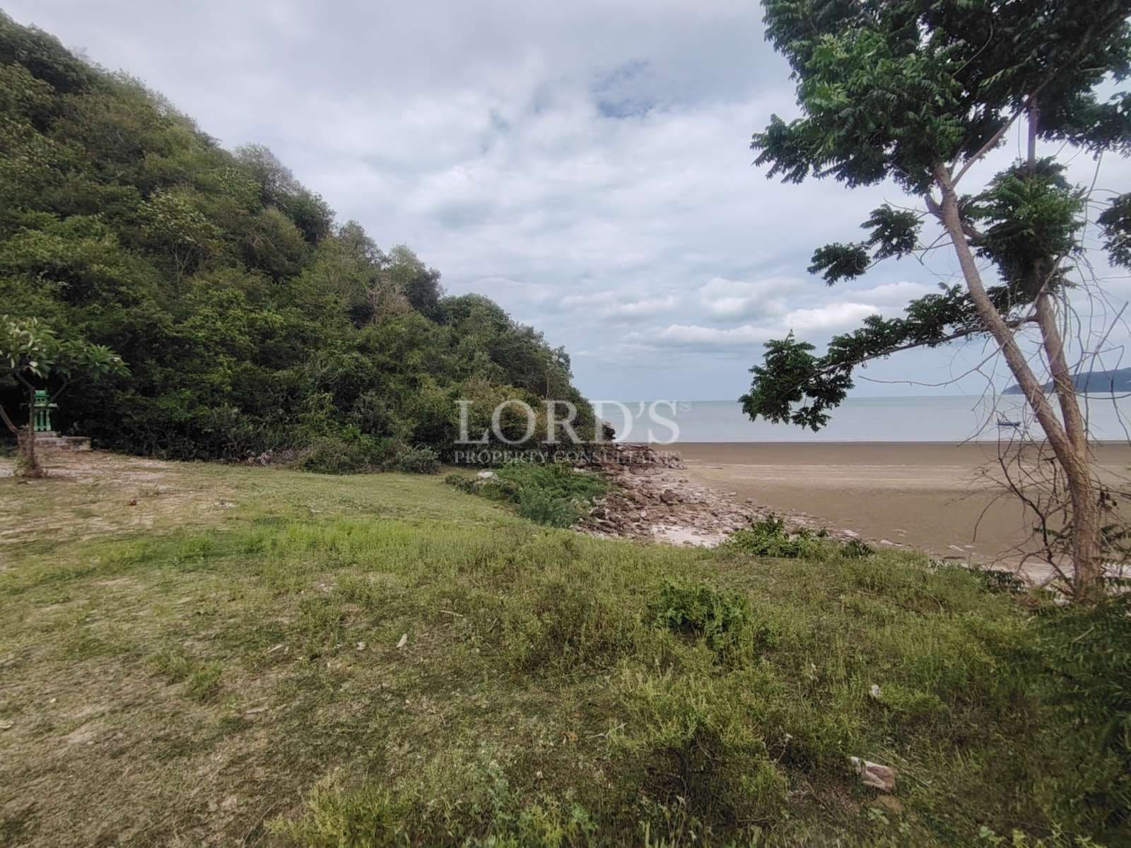 Open coastal land beside a green hillside with a rocky shoreline and calm sea in the background.