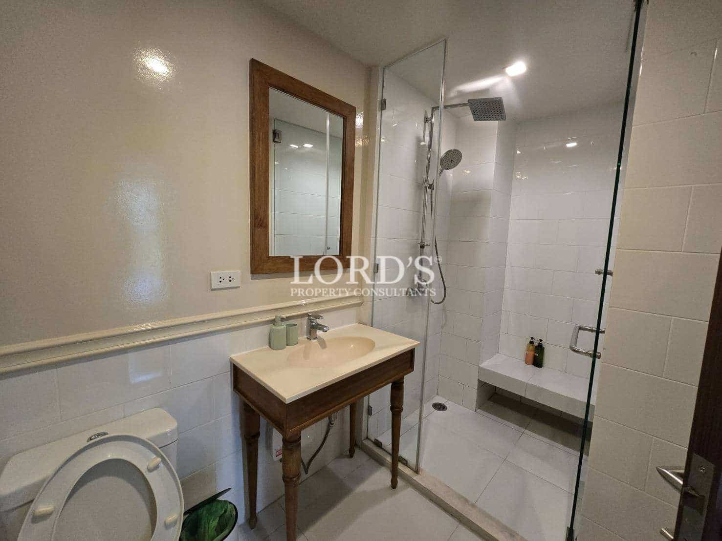 Modern bathroom with wooden vanity sink, wall mirror, toilet, and glass walk-in shower