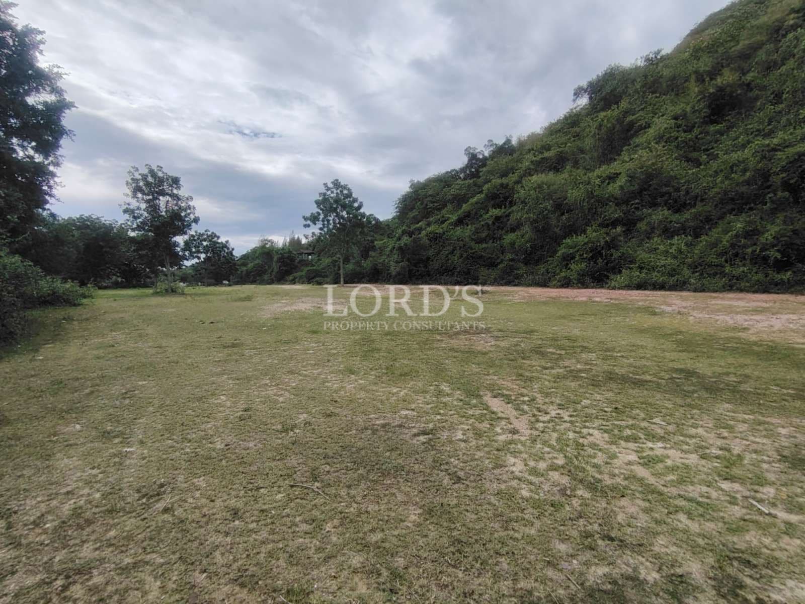 Open grassy land beside a green hillside with scattered trees under a cloudy sky.