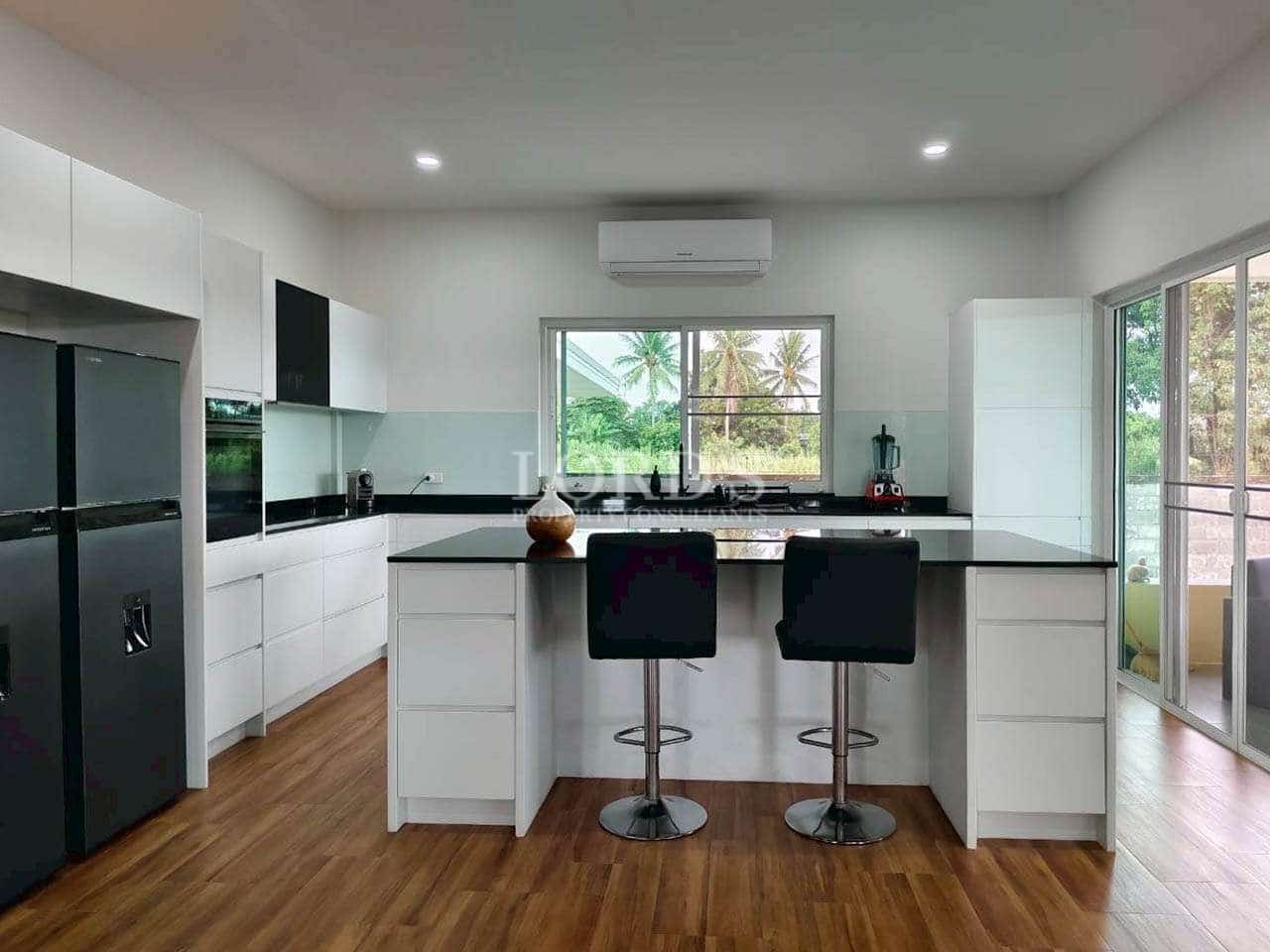 Modern open-plan kitchen with white cabinets, black countertops, island seating, and large window.