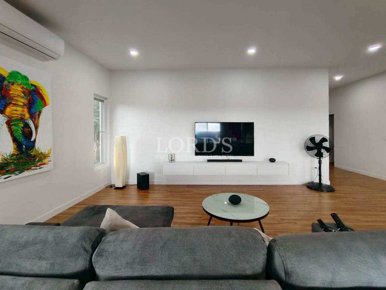 Modern living room with wall-mounted TV, grey sofa, wooden flooring, and contemporary artwork.