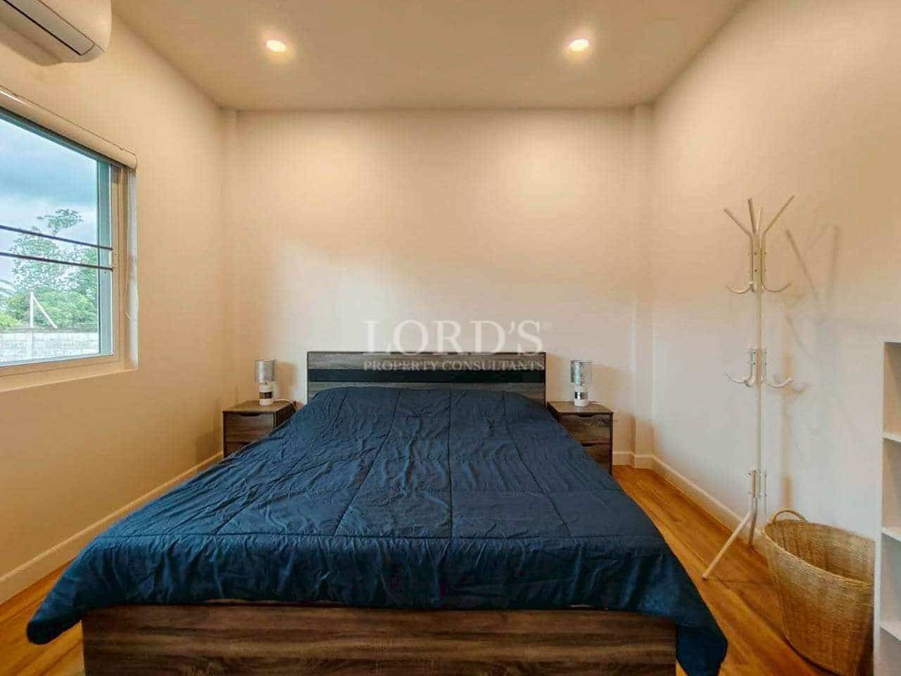 Minimalist bedroom with wooden flooring, double bed, bedside tables, and natural light.