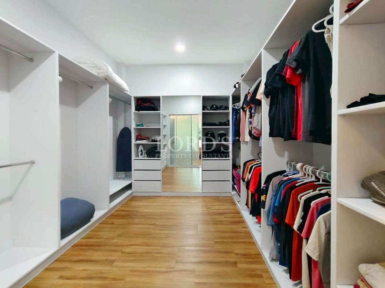 Spacious walk-in wardrobe with built-in shelving, hanging rails, and wooden flooring.