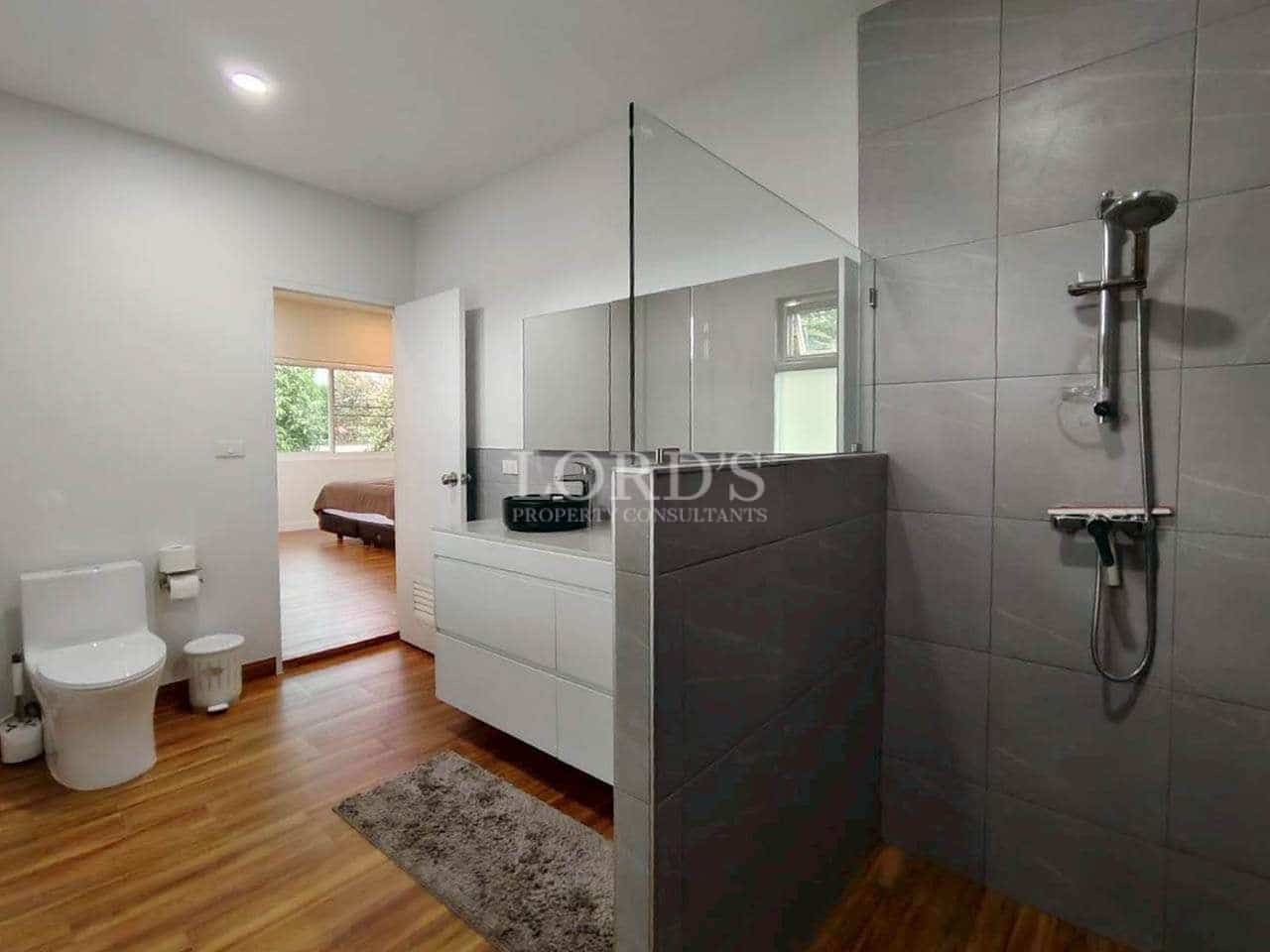 Modern bathroom with walk-in shower, glass partition, floating vanity, gray tiles, and wooden flooring.