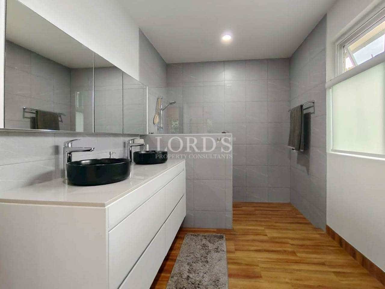 Modern bathroom with double vanity, walk-in shower, gray tiles, and wooden flooring.