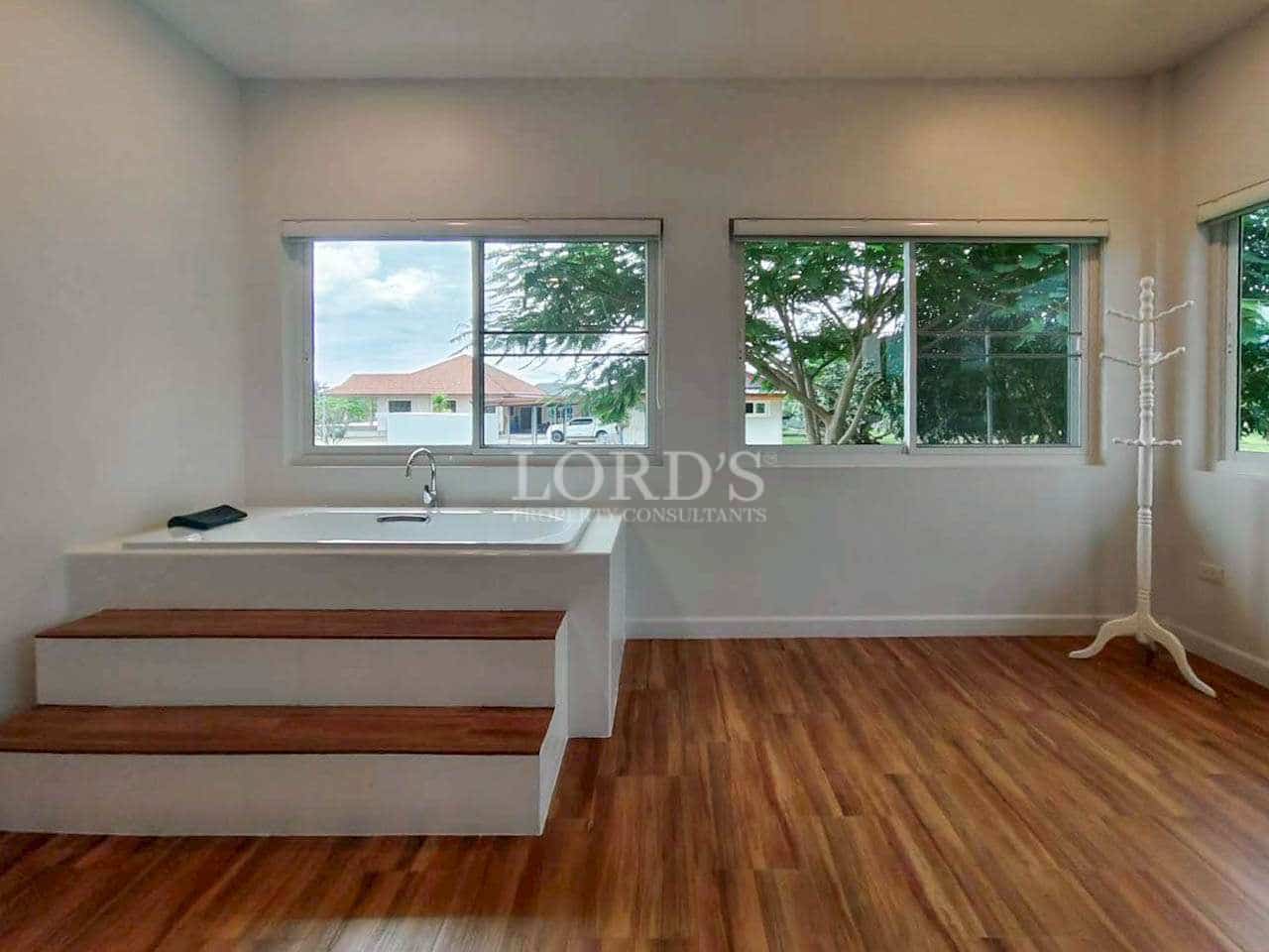 Modern bathroom with soaking tub, wooden flooring, and large windows with garden views.