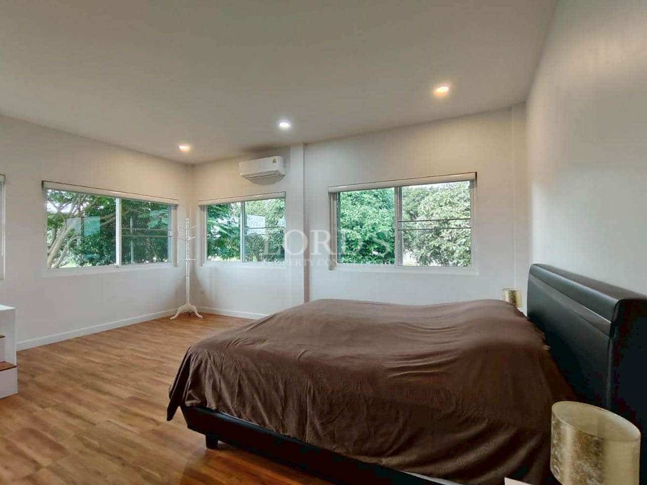 Bright bedroom with wooden flooring, large windows, and natural green views.